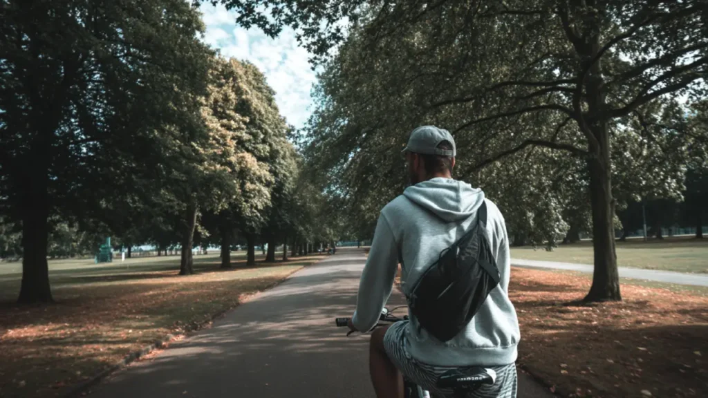 Young man cycling with a fanny pack across his back, enjoying a sunny day in a park